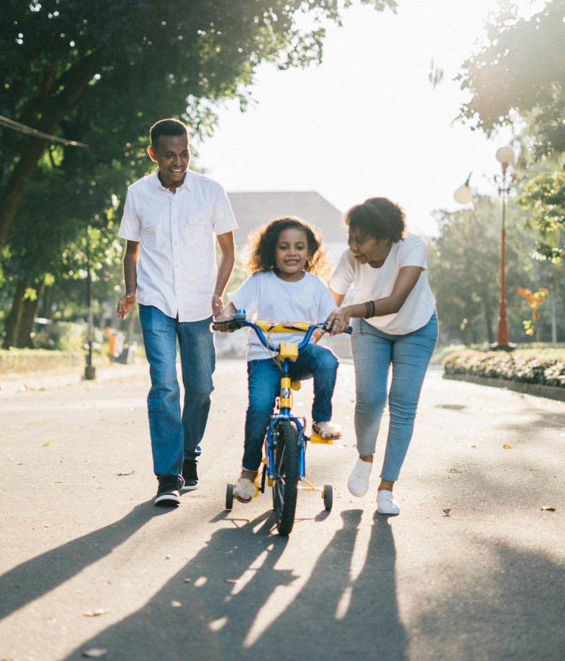 Two parents help their child ride a bike